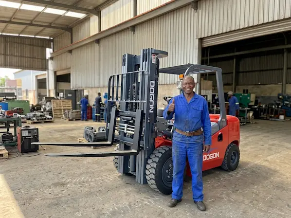 Happy customer giving a thumbs up next to a DOGON diesel forklift in a manufacturing workshop.